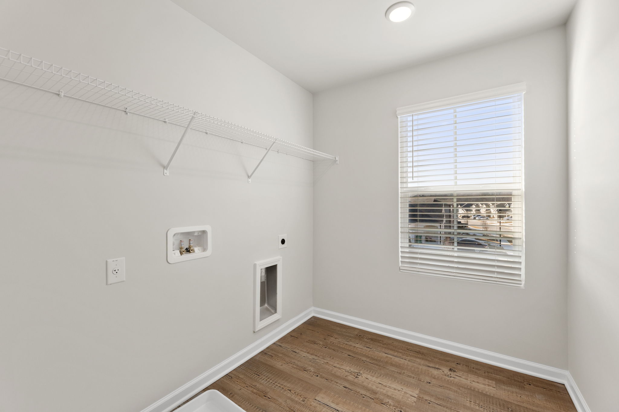 A room with a wood floor and a window with blinds.