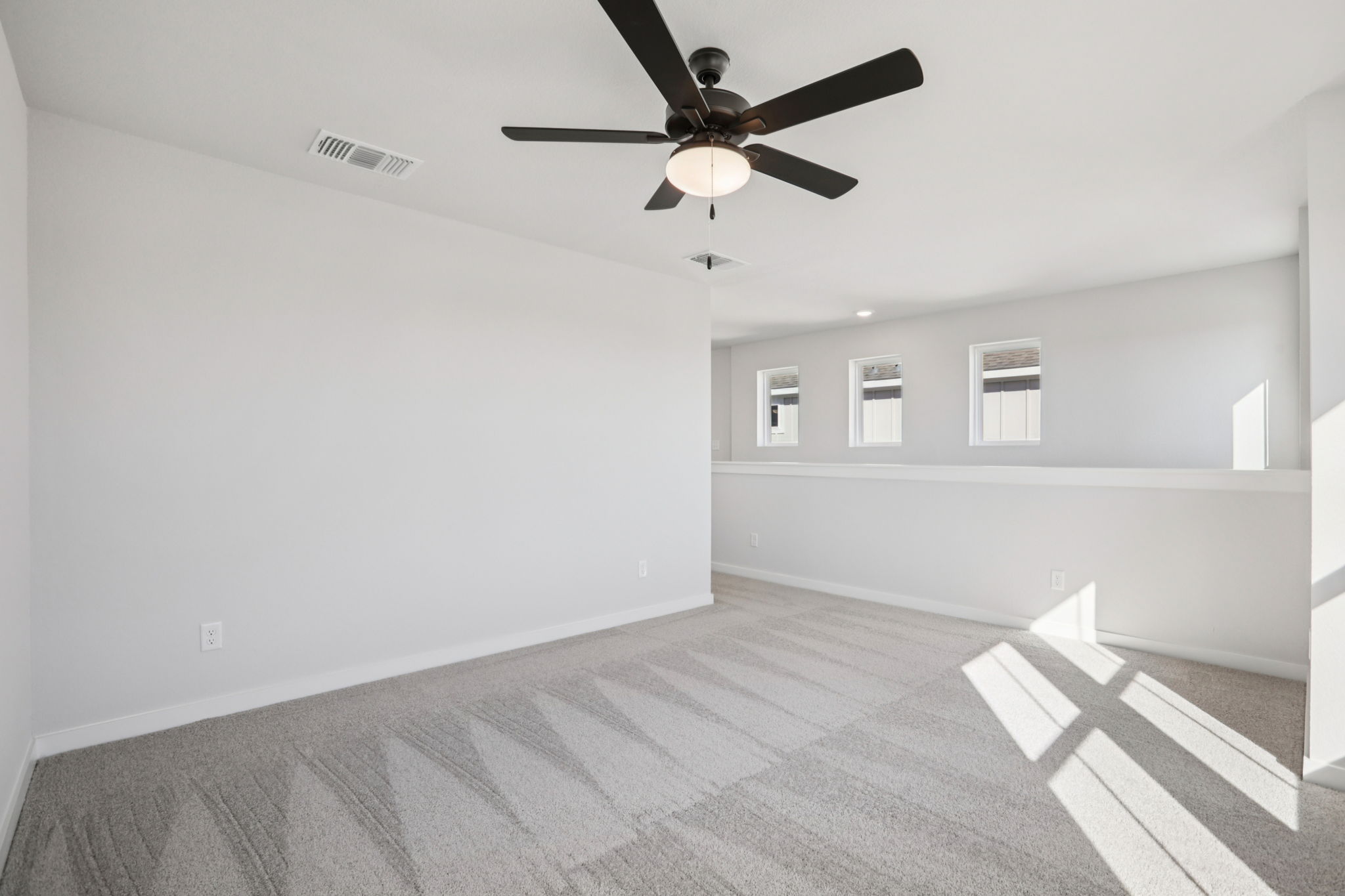 A room with a ceiling fan and a white wall.