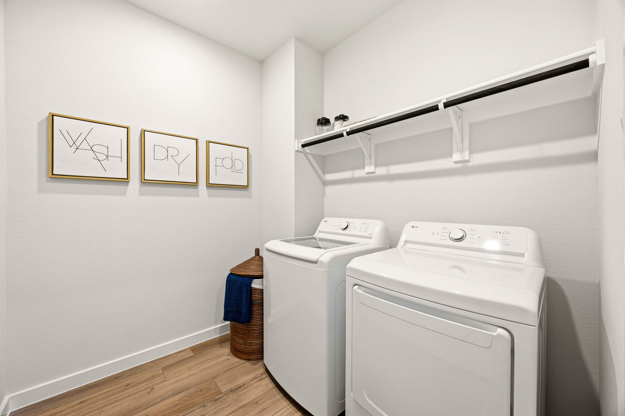 A laundry room with a white laundry machine and a white shelf.