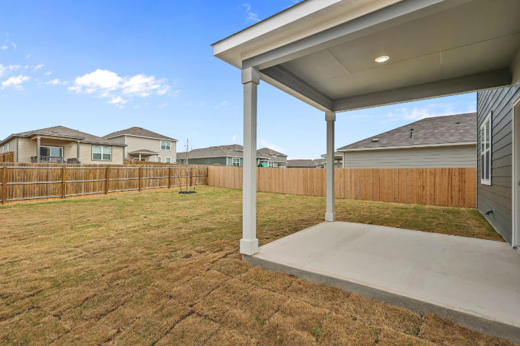 A fenced in yard with a covered area and a building in the background.